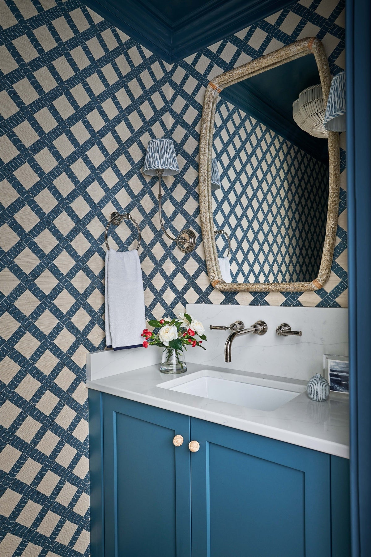 Powder room with a blue shaker-style vanity, white quartz top, and wall-mounted faucet set against blue lattice wallpaper