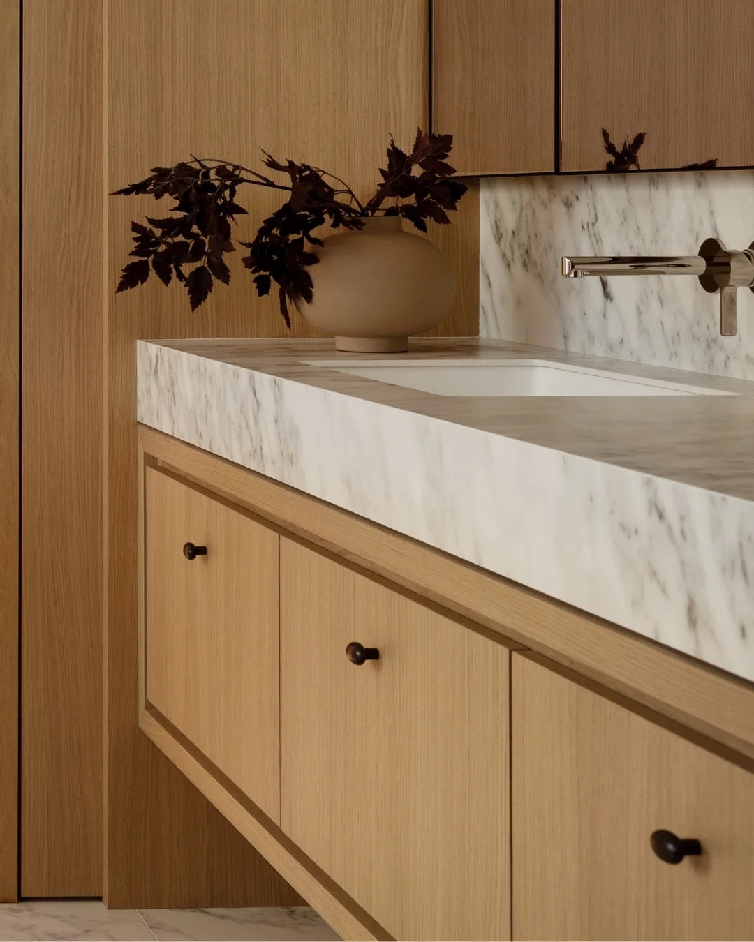 Oak vanity drawers with round dark knobs under a thick marble countertop